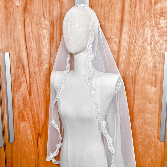 Side view of a floor length mantilla veil with Alençon lace draped over a bridal mannequin.