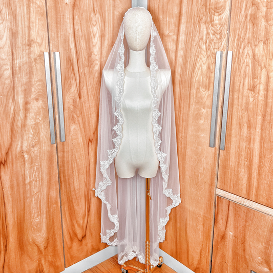 A delicate beaded bridal mantilla veil in waltz length draped elegantly over a bridal mannequin to show its fall and intricate lace edging.