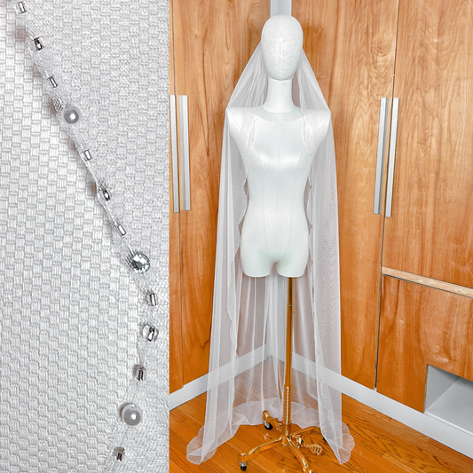 A full-length view of a ivory tulle wedding veil with intricate beaded scalloped edges draped elegantly.
