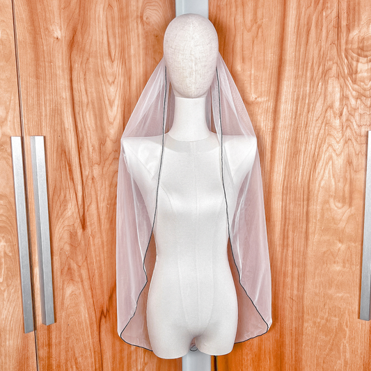 Fingertip length black pencil edge wedding veil displayed on a bridal mannequin.