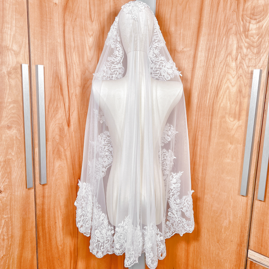 Rear view of a beaded lace mantilla wedding veil in fingertip length, showcasing the scalloped lace border on a mannequin.