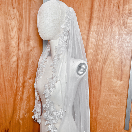 Side profile of a pearl and lace wedding veil in fingertip length, showing how the soft tulle layers sit elegantly on a mannequin headpiece.