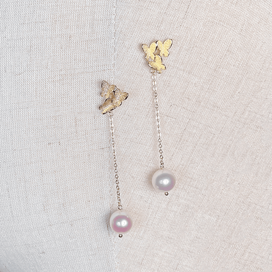 Pair of gold butterfly pearl dangle earrings displayed against a clean white background.