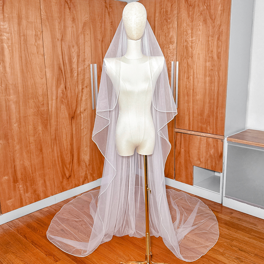 Cathedral length cascade wedding veil with a distinct corded edge displayed on a bridal mannequin.