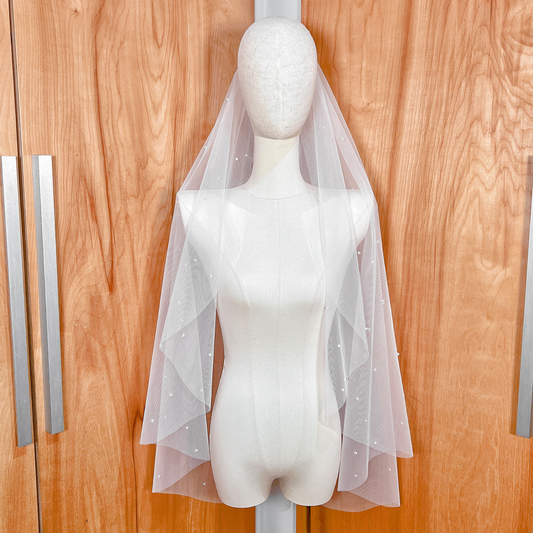 Fingertip length cascading scattered pearl wedding veil with white pearls draped on a mannequin.