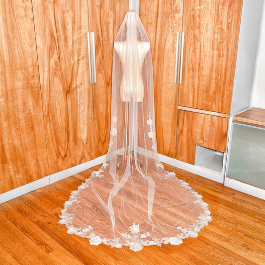 Rear view of a 3D floral lace bridal veil in cathedral length draped over a mannequin to highlight the sheer tulle and floral pattern.
