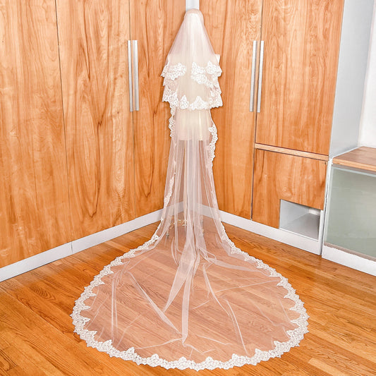 Back view of a cathedral length Alençon lace wedding veil with a two-tier drop blusher draped on a mannequin.