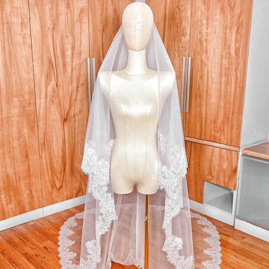 A wide view of the cathedral length Chantilly lace drop wedding veil with blusher fully spread out on a mannequin.