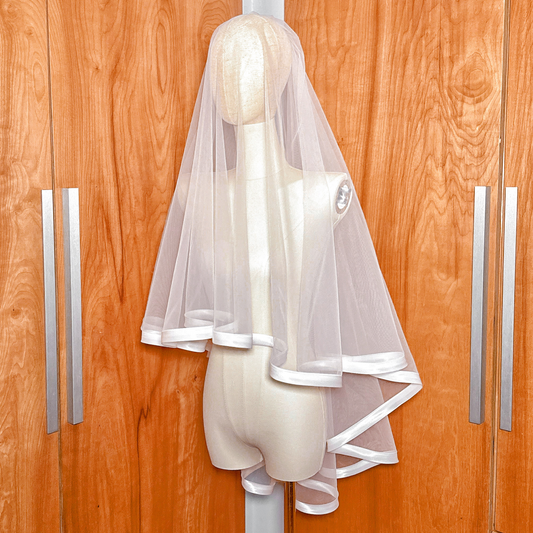 Side profile of a 1-inch ribbon edge wedding veil with blusher in fingertip length on a dress form.