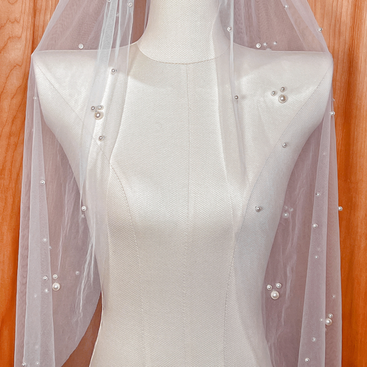 Close-up view of a scattered pearl wedding veil in fingertip length, highlighting the intricate pearl placement and sheer bridal fabric.