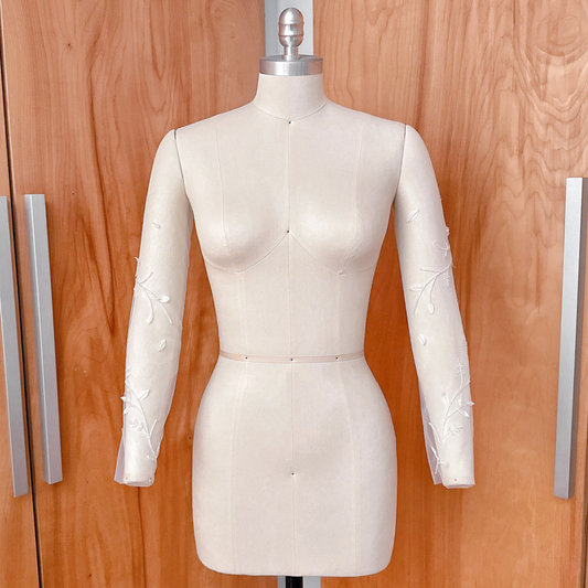 A side-angle studio shot of the beaded floral vine illusion sleeves on a dress form, showcasing the continuous botanical vine design down the length of the arm.