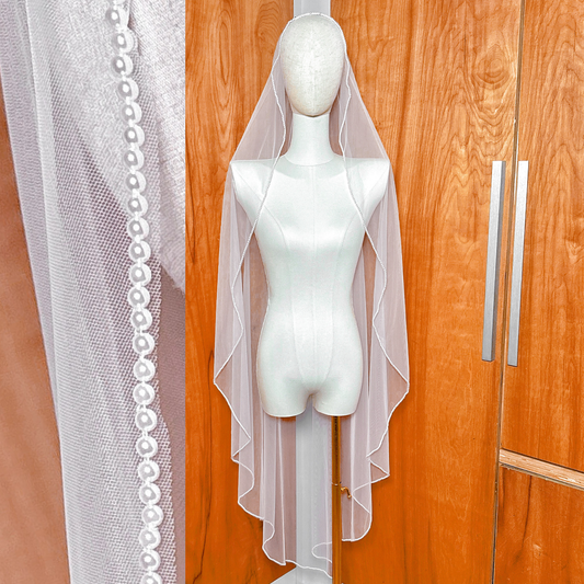 Front view of an ivory pearl mantilla wedding veil draped over a mannequin's head to show how the lace and pearls frame the face.