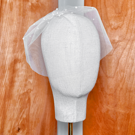 Front view of a white mini birdcage wedding veil with scattered pearls on a display bust.