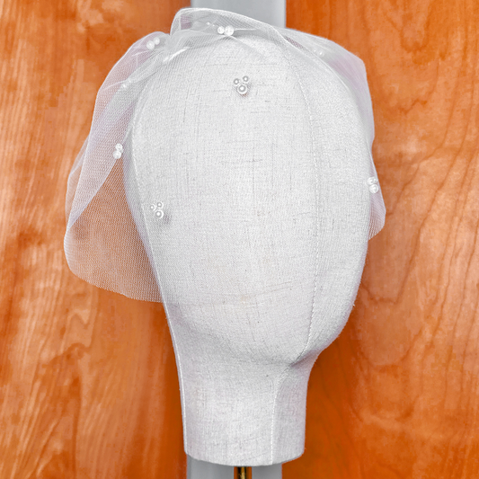 Front view of a mini tulle birdcage wedding veil with trio pearls accenting the mesh.