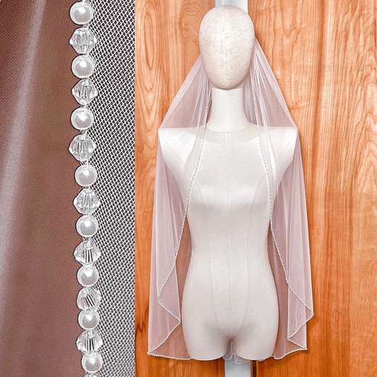 Front view of a sheer fingertip length wedding veil featuring a delicate pearl and crystal beaded edge.