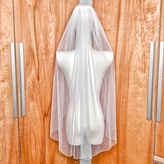 Back view of a fingertip-length wedding veil featuring a hand-sewn pearl beaded trim for a classic bridal look.