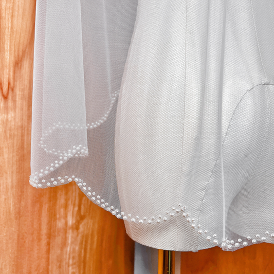 Detailed view of the pearl-edged scalloped trim on a classic fingertip-length wedding veil.