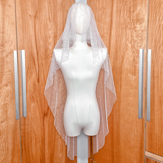 Front view of a knee-length scattered pearl blusher veil displayed on a mannequin, featuring delicate ivory pearls across soft bridal tulle.