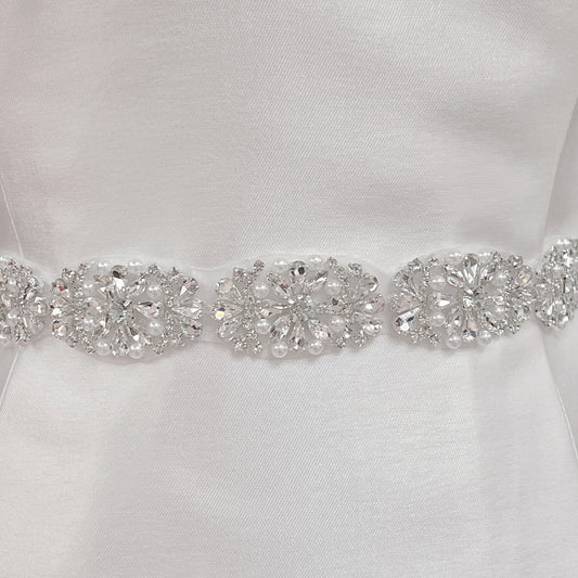 Close-up of a silver rhinestone and pearl bridal belt with intricate beadwork detailing on a dress display.