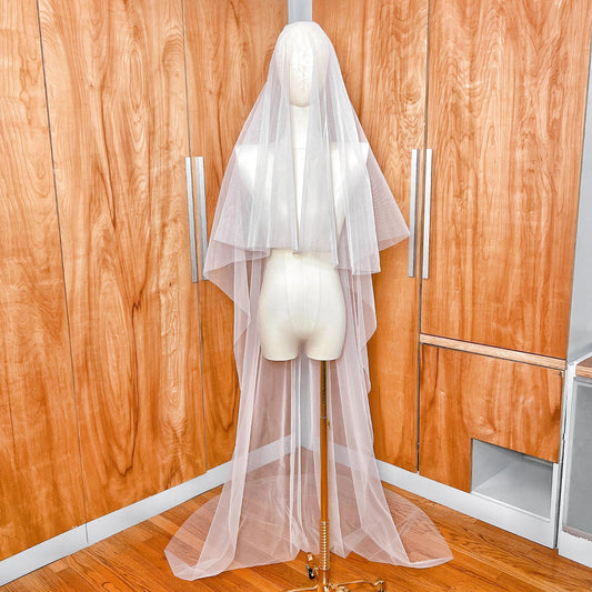 Front view of a simple two-tier chapel length wedding veil with a sheer blusher and minimalist raw edge draping elegantly over a bridal mannequin.
