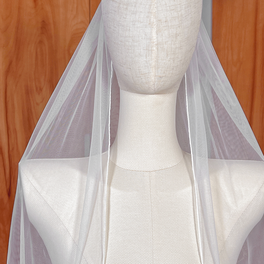 Sheer bridal tulle of a fingertip single tier pencil edge wedding veil on a mannequin.