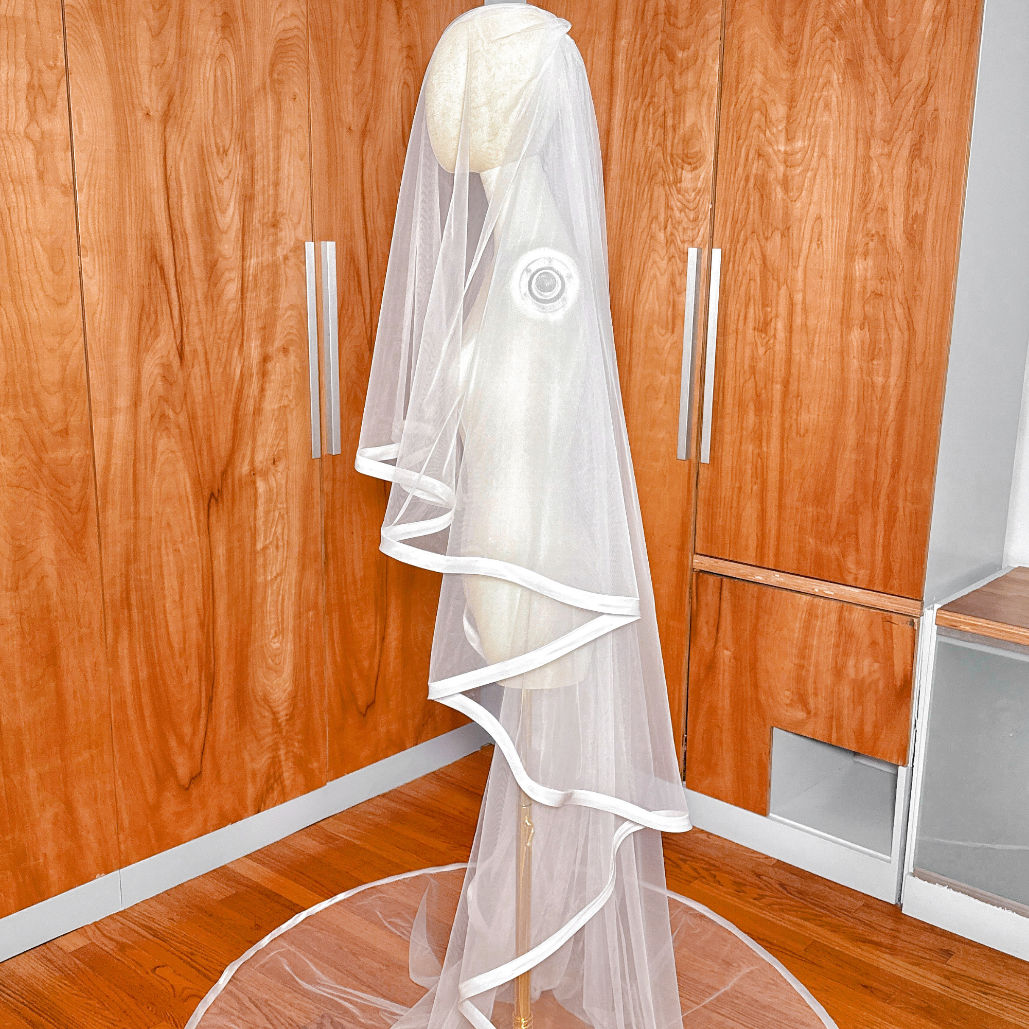 A bridal mannequin displaying a two-tier cathedral length veil with a 1 inch satin ribbon edge and blusher.