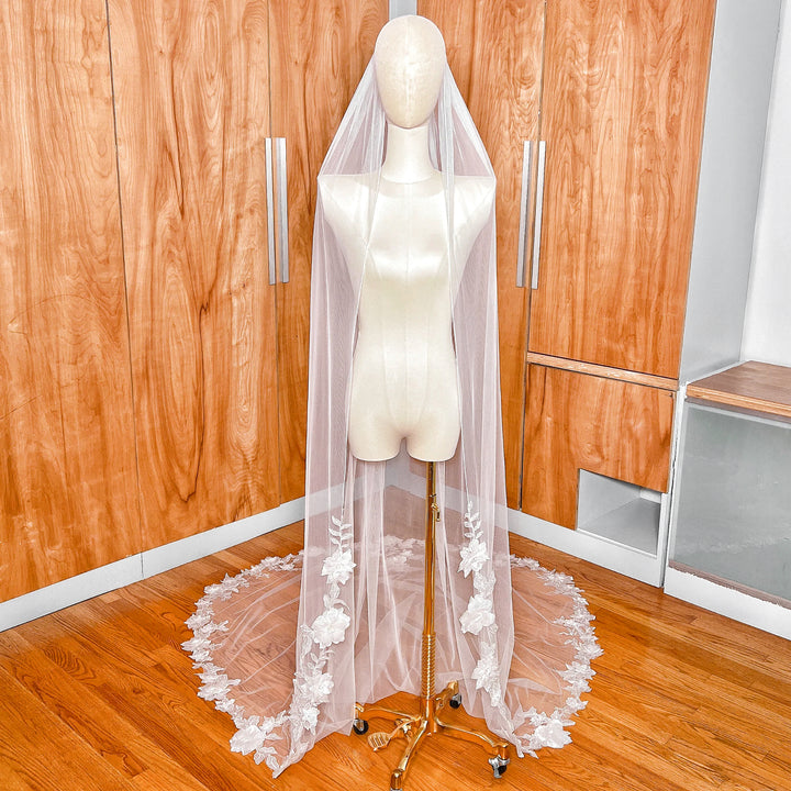 A cathedral-length 3D floral lace wedding veil displayed on a mannequin, showcasing the intricate flower appliqué detail and long train.