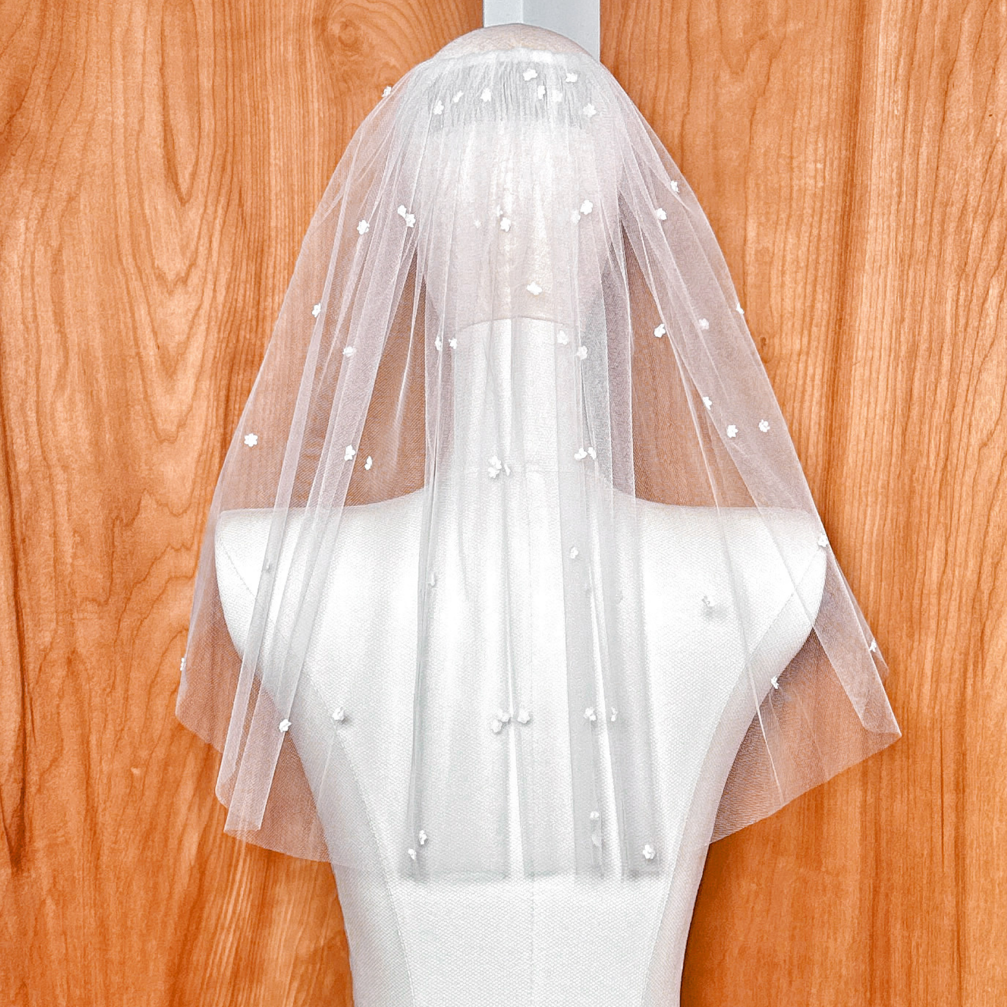 Full back view of the shoulder-length sheer bridal veil draped over a mannequin, showcasing the scattered 3D silk satin flowers.