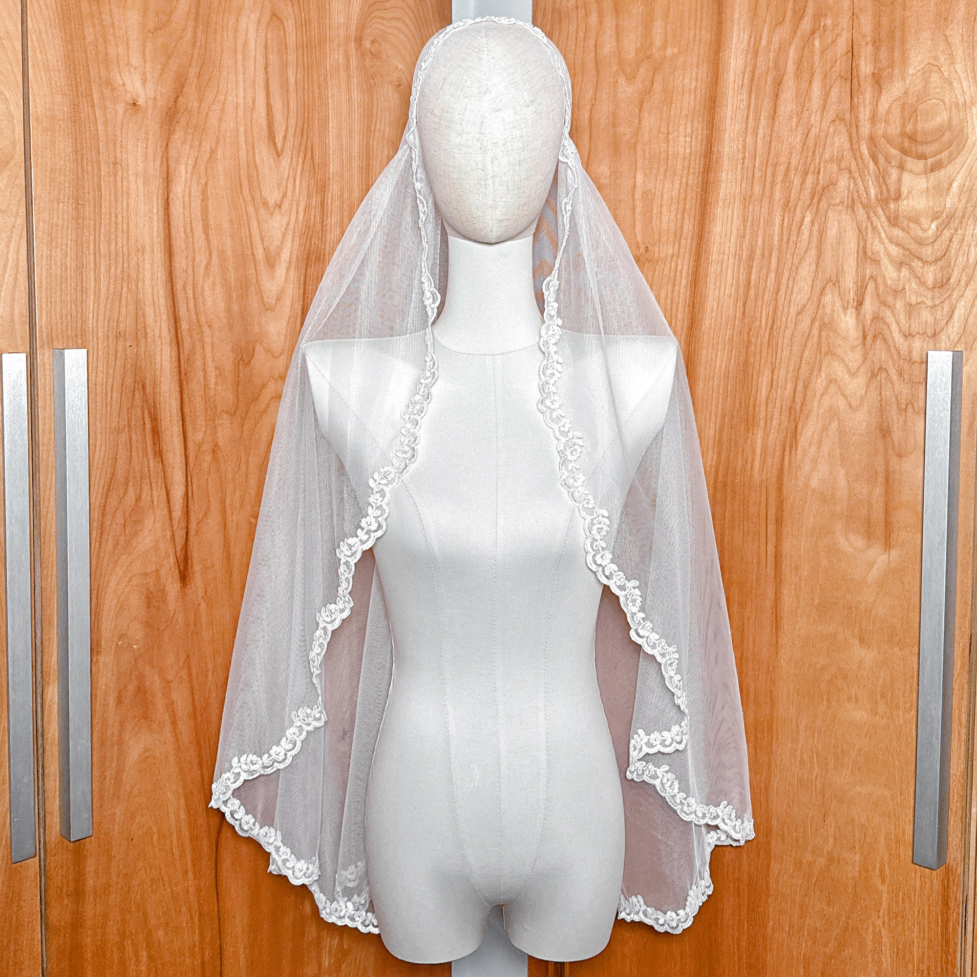 Alençon lace Juliet cap veil in fingertip length displayed on a bridal mannequin.