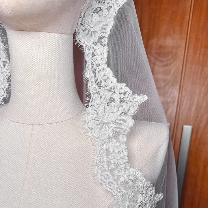 Detail of the Alençon lace framing the face of a mannequin for a traditional mantilla wedding look.