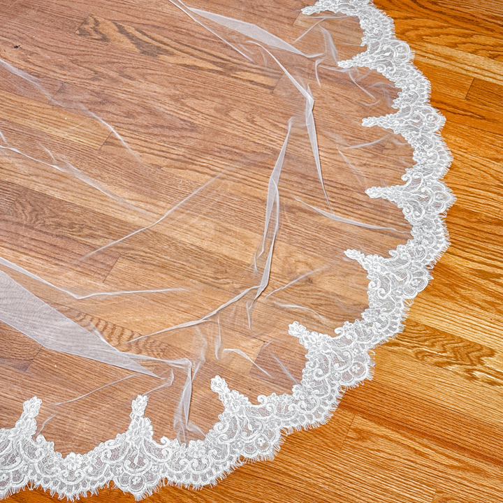 Low-angle shot of the cathedral length train of an Alençon lace mantilla veil resting on the floor.