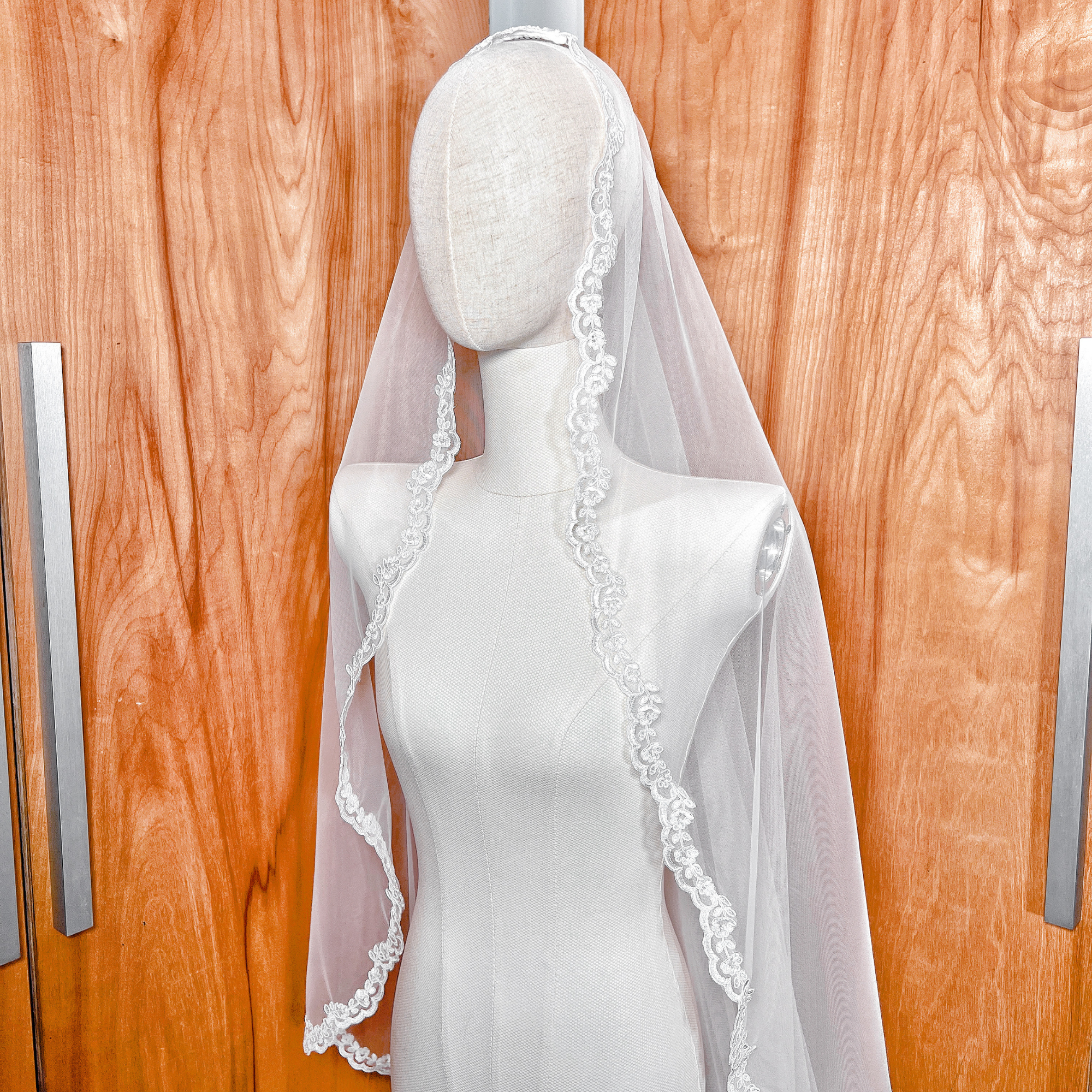 Side view of a floor length mantilla veil with Alençon lace draped over a bridal mannequin.