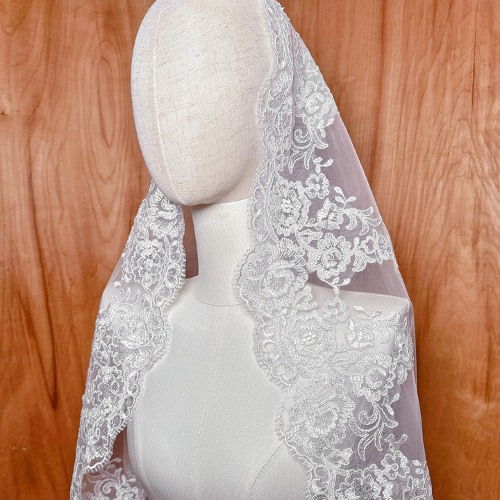 Three-quarter view of the Alençon lace mantilla wedding veil in waltz length, showcasing how the lace-trimmed tulle drapes naturally over the mannequin's shoulders.