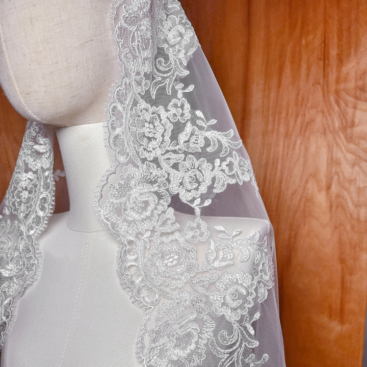 Sheer bridal illusion tulle on a waltz-length Alençon lace mantilla wedding veil draped over a mannequin to show transparency.