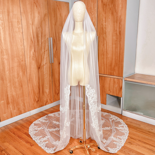Cathedral length Alençon lace wedding veil draped elegantly on a mannequin, showcasing the intricate scalloped lace trim and flowing tulle.