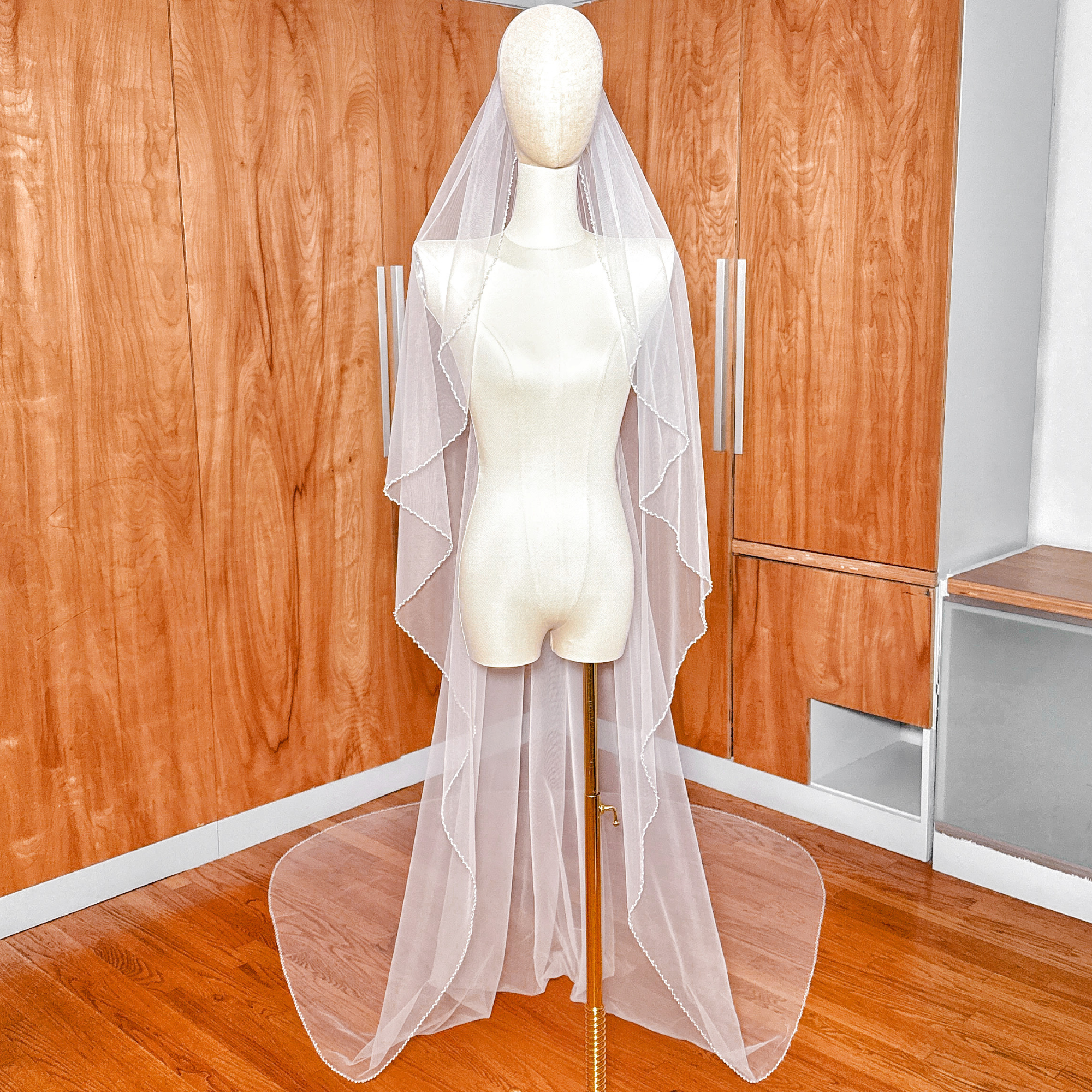 A cathedral-length angel cut pearl trim wedding veil draped elegantly over a bridal form.
