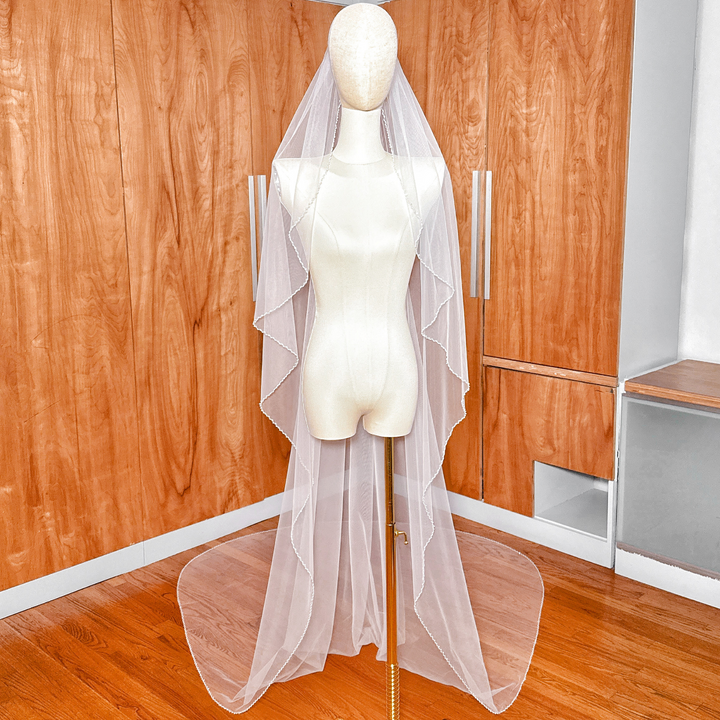 A cathedral-length angel cut pearl trim wedding veil draped elegantly over a bridal form.