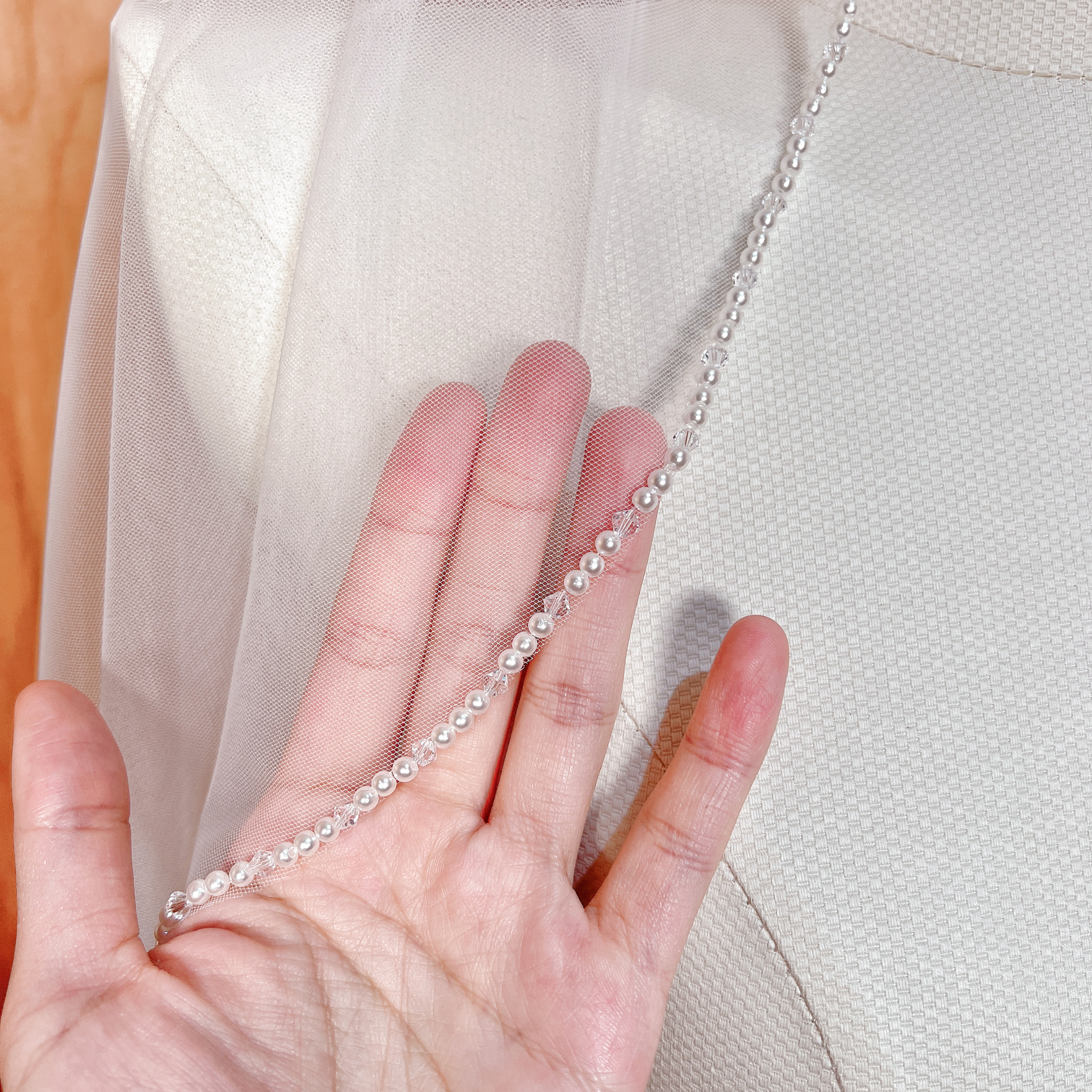Close up detail of the pearl trim on the edge of a waltz length angel cut wedding veil, highlighting the bridal tulle texture.