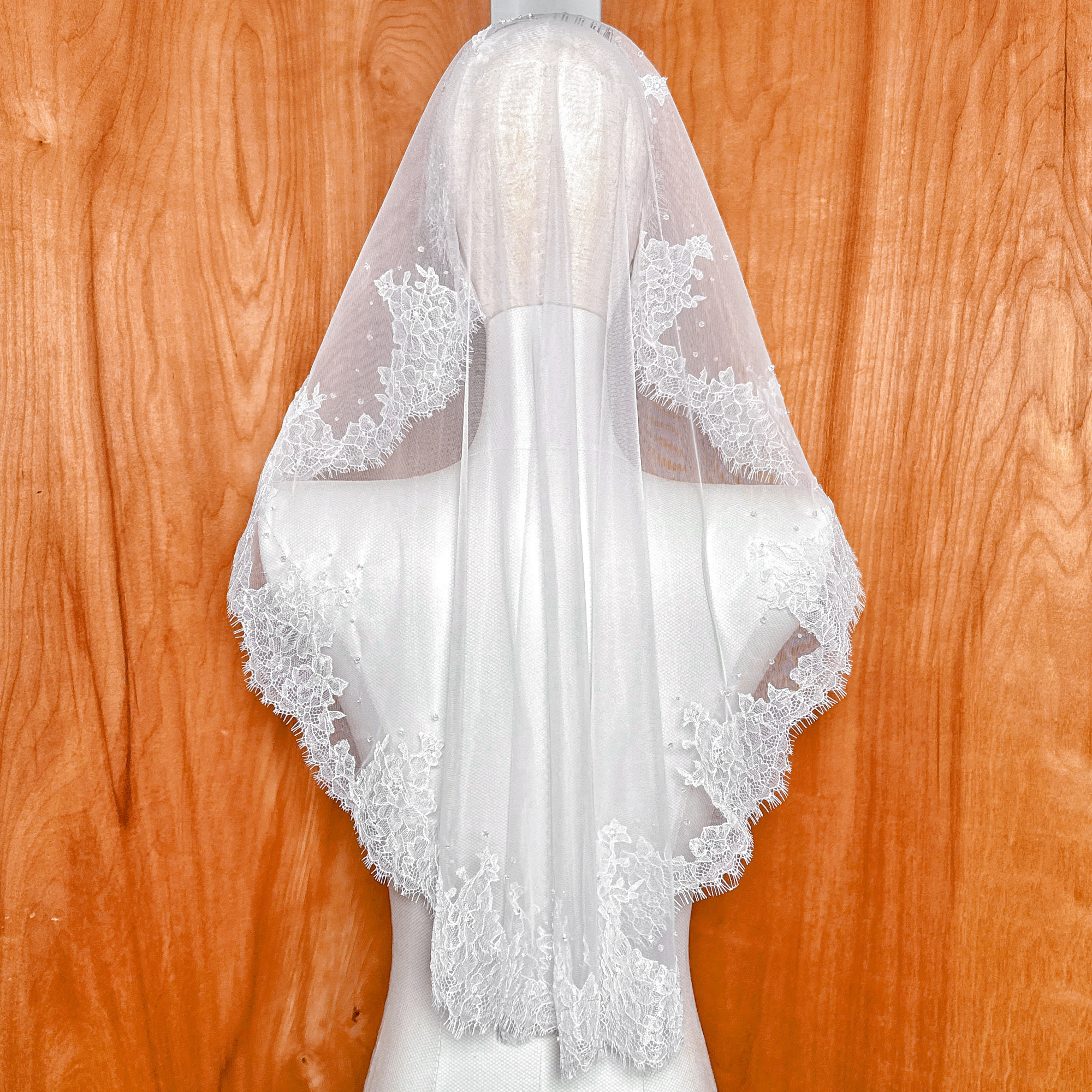 Back of an ivory Chantilly lace mantilla veil at elbow length draped over a mannequin's head.