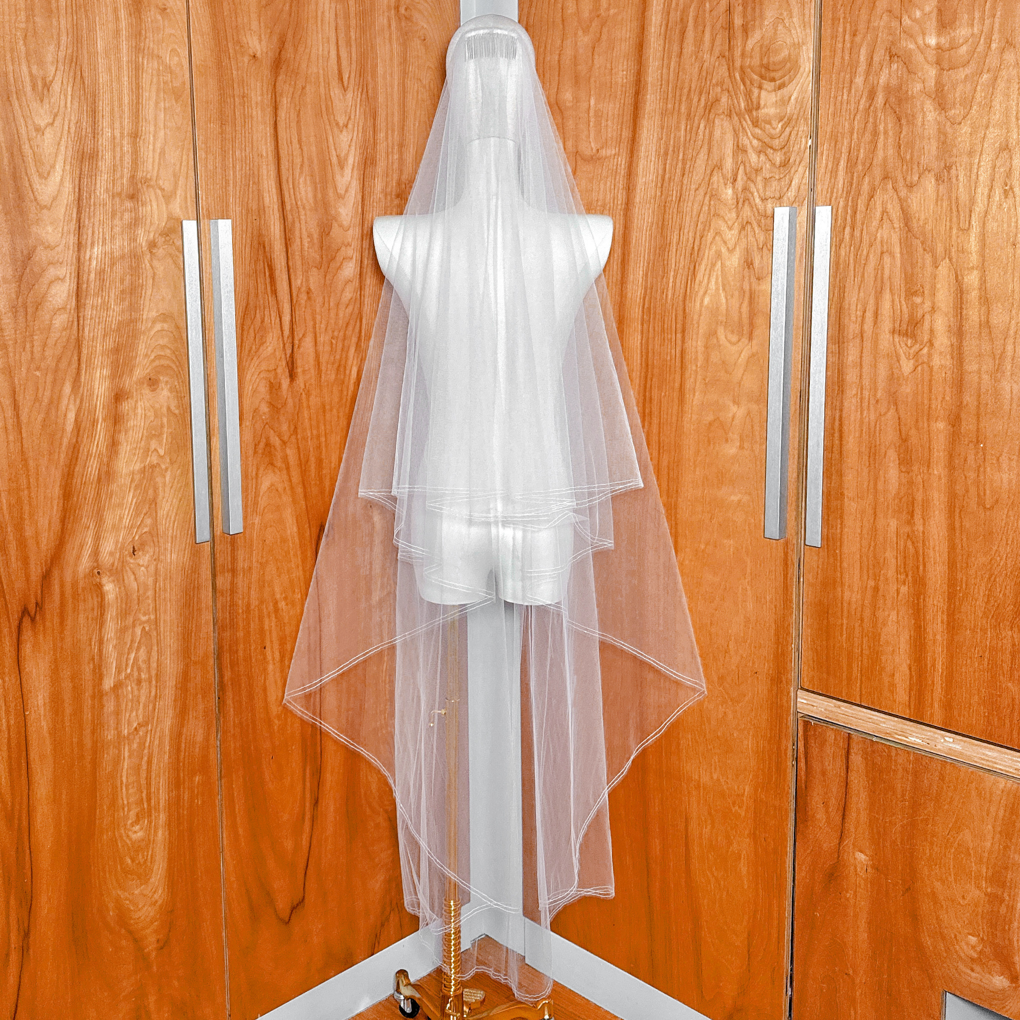 Rear view of a waltz length two tier wedding veil with a pencil edge and blusher hanging elegantly on a mannequin.