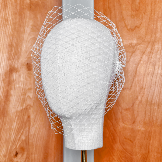 Front view of a white bandeau birdcage wedding veil displayed on a mannequin.