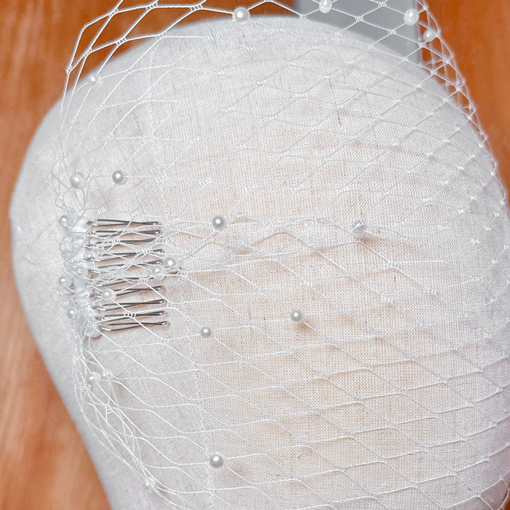 Close-up of a white tulle bandeau birdcage wedding veil with pearls scattered across the netting.