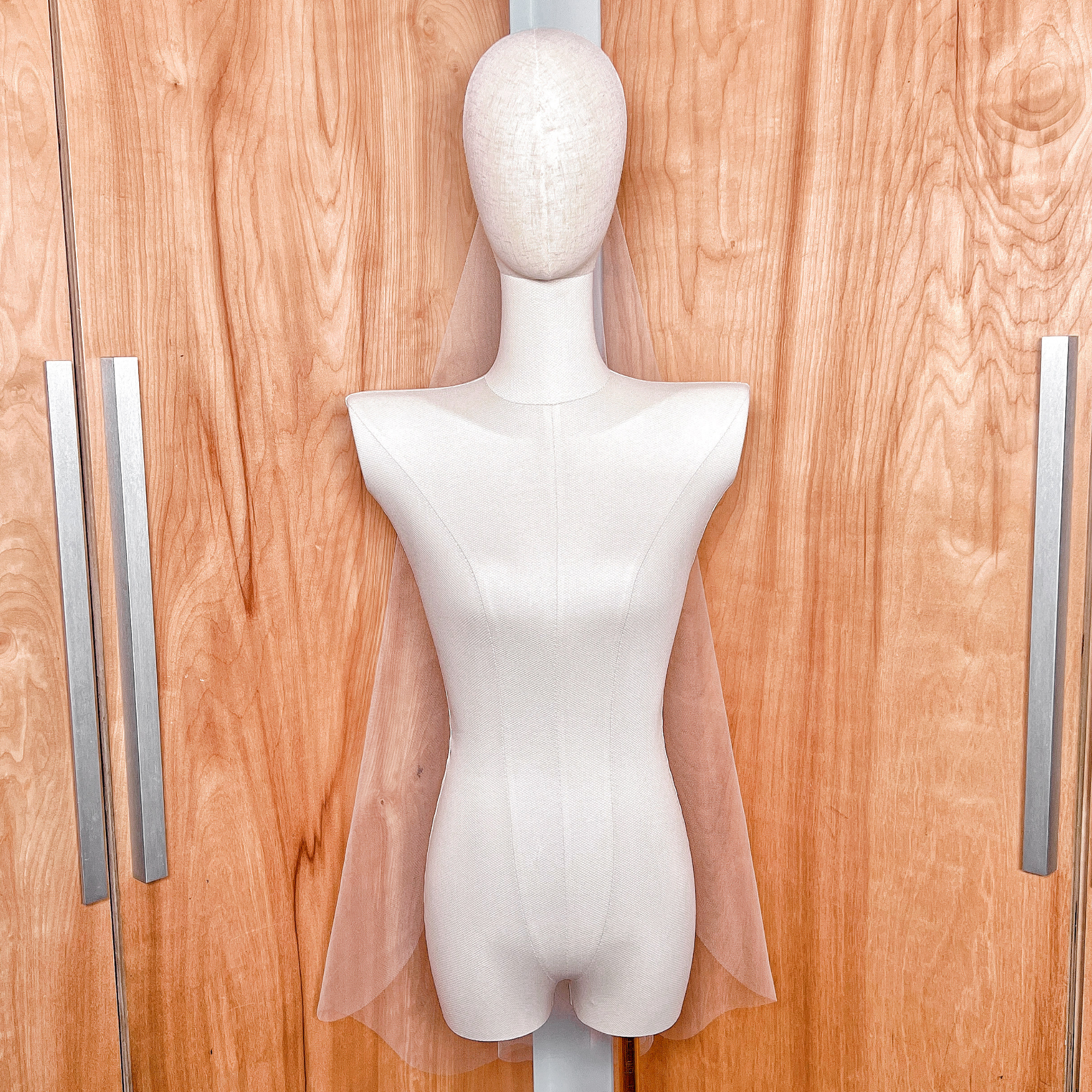 A sheer, barely there fingertip-length wedding veil with a clean raw edge shown draping elegantly over a mannequin's shoulders.