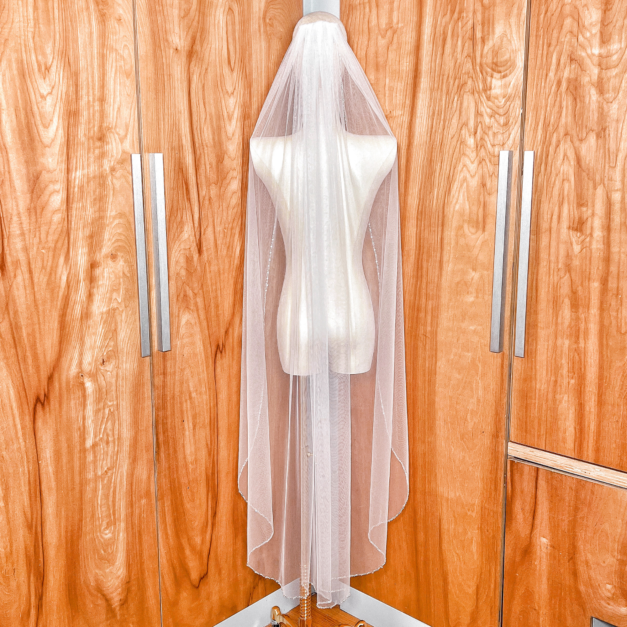 Back view of a waltz length beaded edge wedding veil on a dress form.
