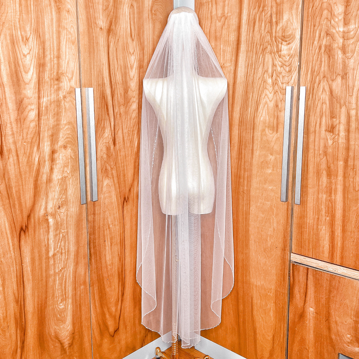 Back view of a waltz length beaded edge wedding veil on a dress form.