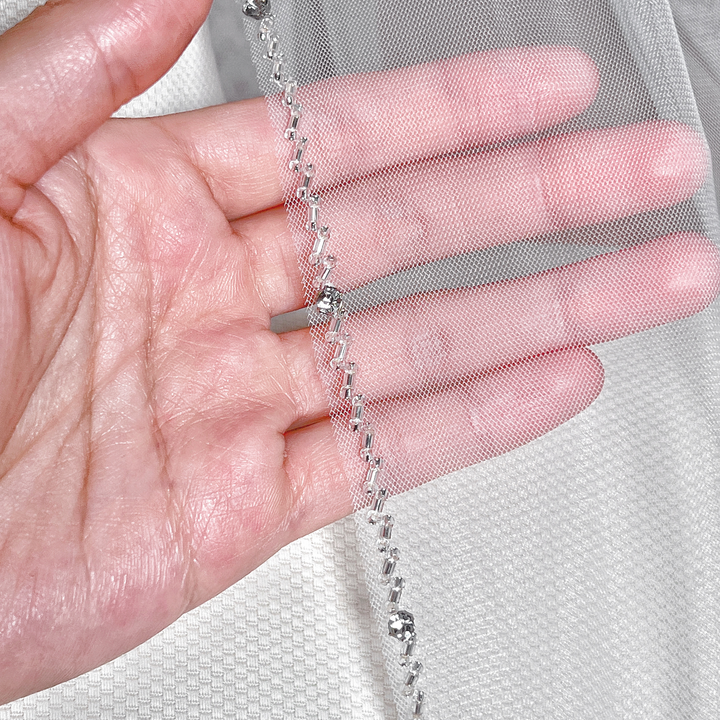 Close-up view of the intricate crystal and beadwork along the edge of a sheer bridal veil.