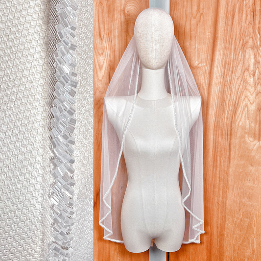 Fingertip length beaded edge wedding veil with frosted bugle beads displayed on a bridal mannequin.