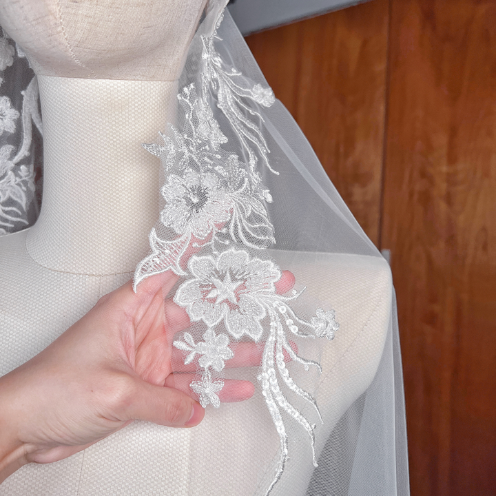 Close-up of the scalloped floral lace edge on a beaded lace mantilla wedding veil with shimmering hand-beaded details.