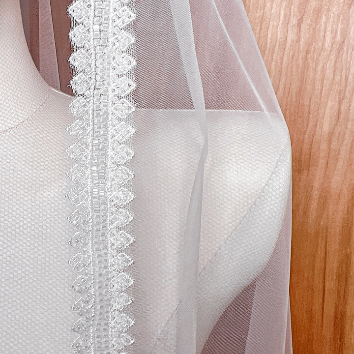 Close-up detail of the intricate hand-sewn beads and sequins on the edge of the beaded mantilla wedding veil.
