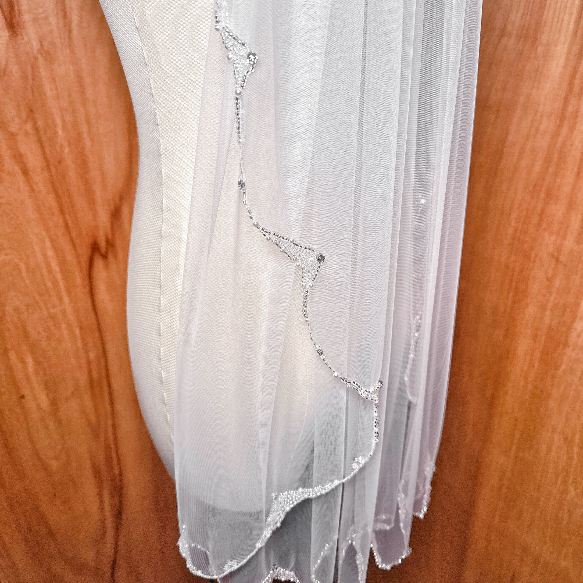A classic fingertip length wedding veil with a pearl-embellished edge showing a graceful, airy drape.